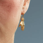 Model wearing a hand-shaped earring with an emerald in sterling silver with 18k gold plating