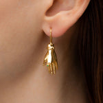 Model wearing a sterling silver earring with 18k gold plating and an emerald in the shape of a hand