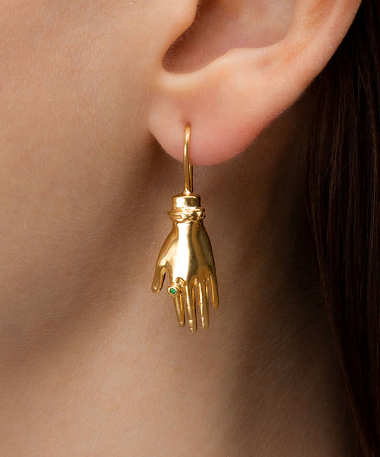 Model wearing a sterling silver earring with 18k gold plating and an emerald in the shape of a hand