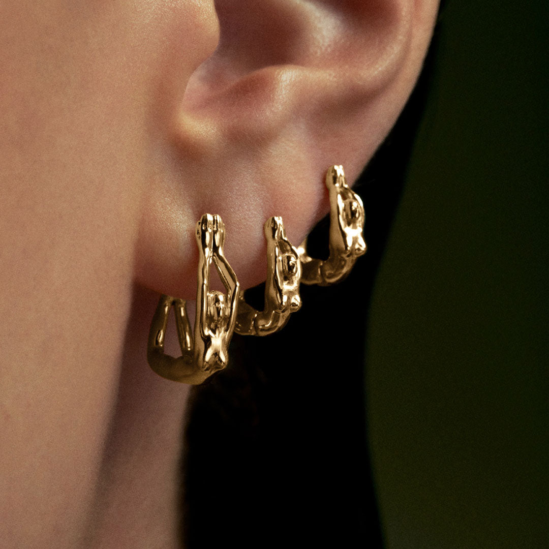 Model wearing earrings and a female body piercing in 18k gold