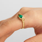 Model wearing 18k gold hands ring adorned with diamonds and an oval emerald