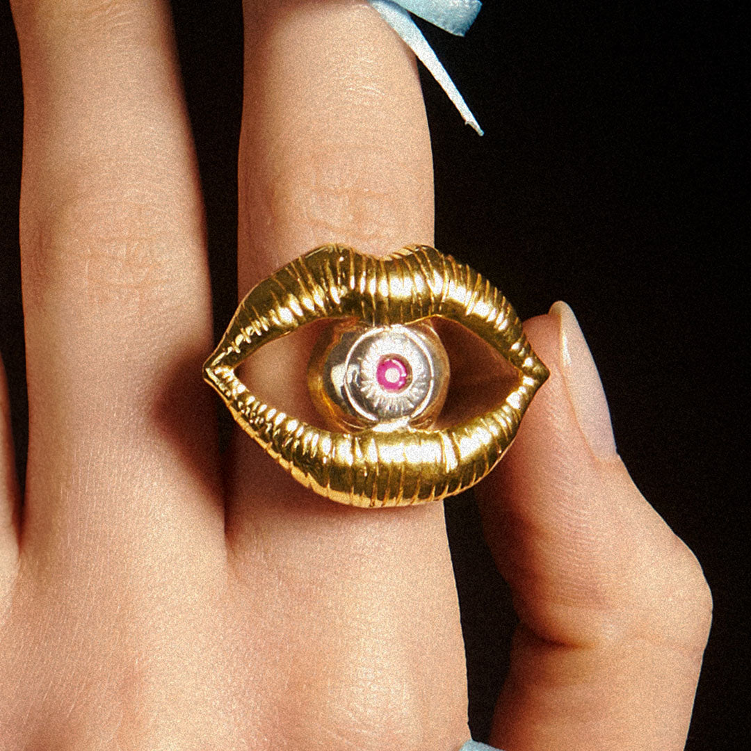 Model wearing a sterling silver ring with 18k gold plating of a mouth and eye with a ruby